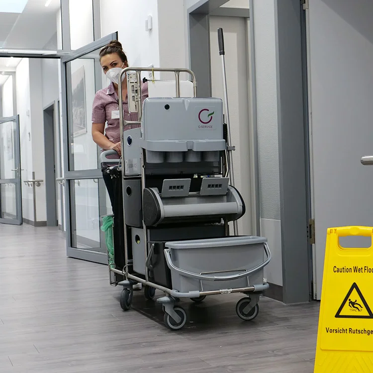 Frau die einen Reinigungswagen durch den Gang fährt